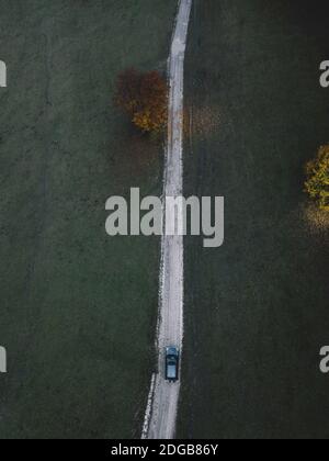 Luftaufnahme der Straße mit suv-Auto im Herbstwald. Landschaft mit Landstraße, Bäumen mit roten und orangefarbenen Blättern. Draufsicht. Stockfoto