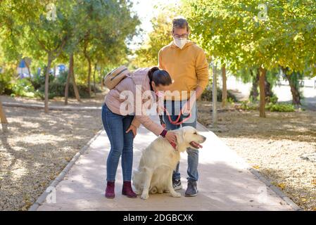 Junge weiße Paar in medizinischen OP-Masken hält Spaziergänge mit Hund im Sommerwald. Familie, europa, Umarmungen, Coronavirus, Krankheit, Infektion Stockfoto