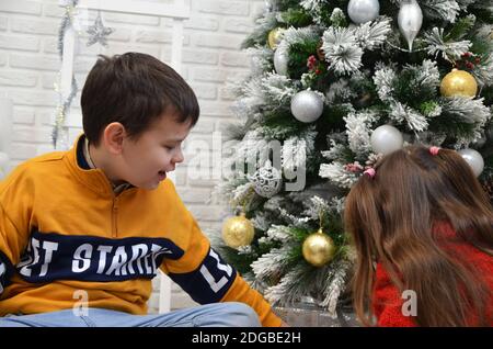 Glückliche kleine Kinder schmücken Weihnachtsbaum in schönen Wohnzimmer mit traditionellen Kamin. Kinder Eröffnung Geschenke am Weihnachtsabend. Offene Geschenke, pla Stockfoto