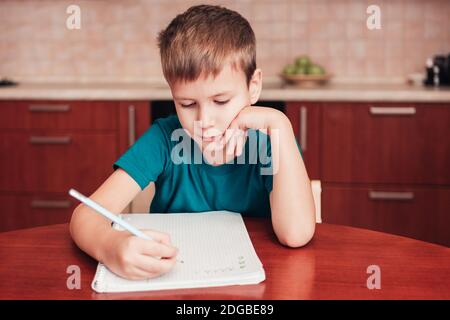 Netter Junge Schreiben Buchstaben im Notizbuch sitzend durch Tisch innen Küche Stockfoto