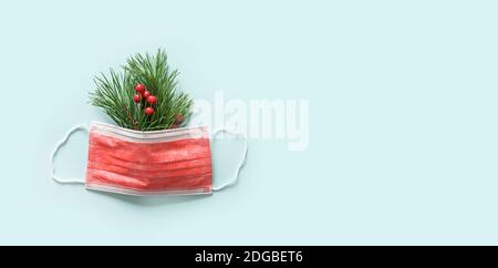 Weihnachtskonzept der roten schützenden medizinischen Gesichtsmaske und immergrünen Ästen auf blauem Hintergrund. Urlaubsbanner mit Platz für die Kopie. Draufsicht. Stockfoto