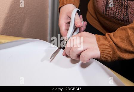 Junges Mädchen schneidet goldenes Geschenkpapier mit weißer Schere Auf einem Tisch mit schwarzem Hintergrund Stockfoto