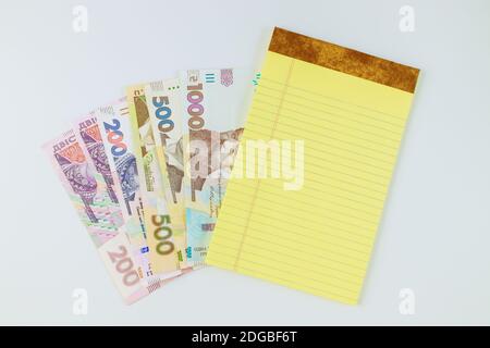 Viele neue Banknoten Ukrainische Griwna im gelben Notizbuch auf Weißer Hintergrund Stockfoto