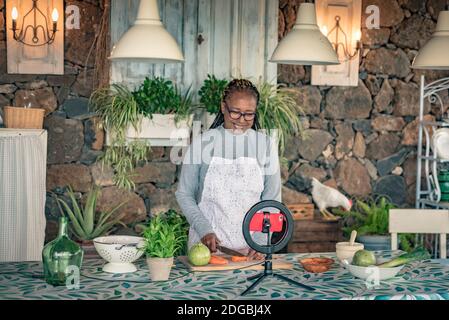 Schwarze Frau mit Brille lehrt online mit ihrem Handy Kochkurse von zu Hause Stockfoto