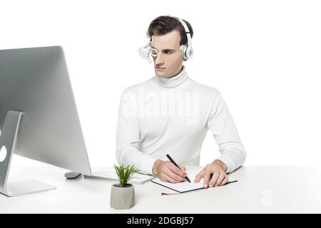 Cyborg Mann in Augenlinse und Kopfhörer Schreiben auf Notebook In der Nähe von Computer und Anlage auf Weiß isoliert Stockfoto