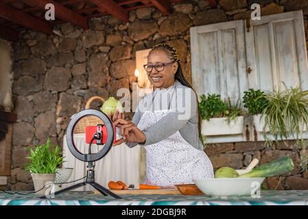 Schwarze Frau mit Brille lehrt online mit ihrem Handy Kochkurse von zu Hause Stockfoto