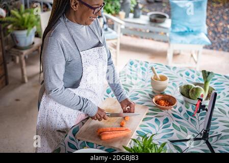 Schwarze Frau mit Brille lehrt online mit ihrem Handy Kochkurse von zu Hause Stockfoto