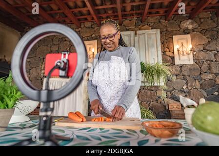 Schwarze Frau mit Brille lehrt online mit ihrem Handy Kochkurse von zu Hause Stockfoto