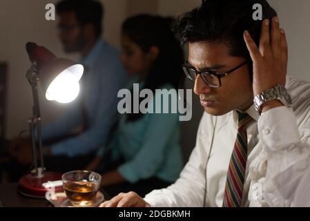Ein indischer Bengali groß, dunkel, hübsch Brünette junge Mann / telecaller in Bürokleidung sitzt auf Bürotisch in Arbeitsstimmung in einem Büro Stockfoto