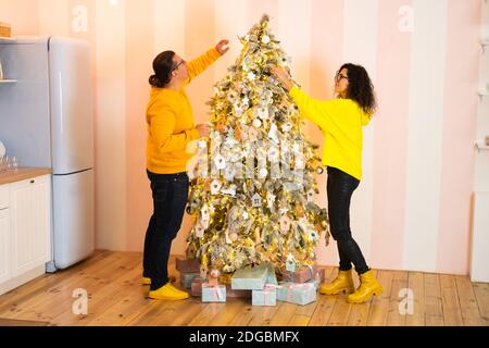 Seitenansicht von Mann und Frau in ähnlich lebhaften Outfits Dekorieren Nadelbaum zusammen am Weihnachtstag in der gemütlichen Küche Zu Hause Stockfoto
