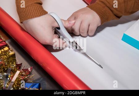 Junges Mädchen schneidet rotes Geschenkpapier mit weißer Schere an Ein Tisch mit schwarzem Hintergrund Stockfoto