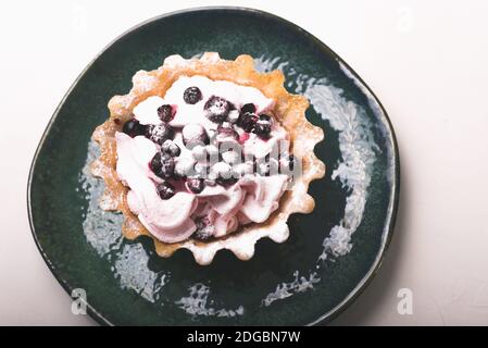 Foto von einem Tartlet mit Beeren und Schlagsahne auf einem grünen Teller auf weißem Hintergrund. Stockfoto