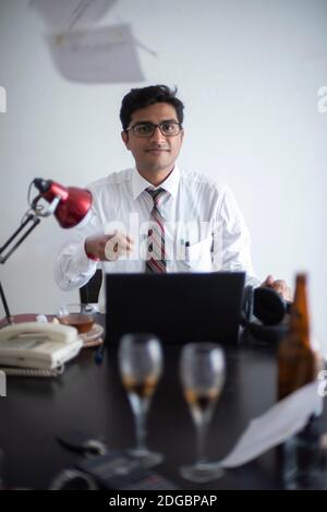 Indische Bengali groß, dunkel, hübsch Brünette junge Mann im Büro tragen genießen Erfolg, während auf einem Bürotisch in einem Büro / bpo sitzen Stockfoto
