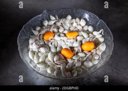 Vier Kumquats und kleine Zwiebeln in Glasplatte. Auf alte Metallplatte geschossen. Mischung aus gesunden Zutaten. Spotlights Studioaufnahme. Stockfoto