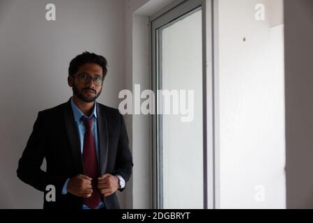 Portrait eines indischen Bengali großer, dunkler, hübscher Brünette junger Mann in Bürokleidung steht vor einem Glasfenster in einem Firmenbüro/bpo Stockfoto