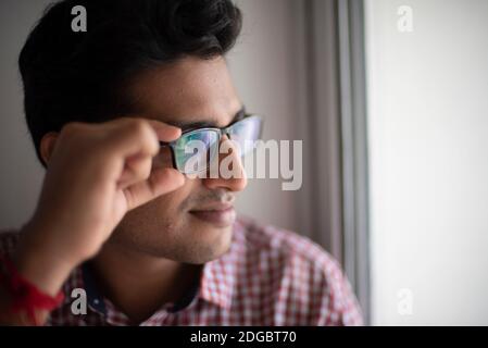 Portrait eines indischen Bengali großer, dunkler, hübscher Brünette junger Mann in Bürokleidung steht vor einem Glasfenster in einem Firmenbüro/bpo Stockfoto