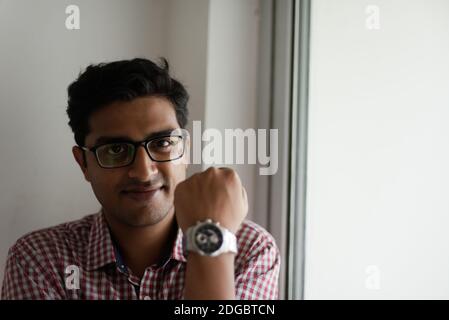 Portrait eines indischen Bengali großer, dunkler, hübscher Brünette junger Mann in Bürokleidung steht vor einem Glasfenster in einem Firmenbüro/bpo Stockfoto