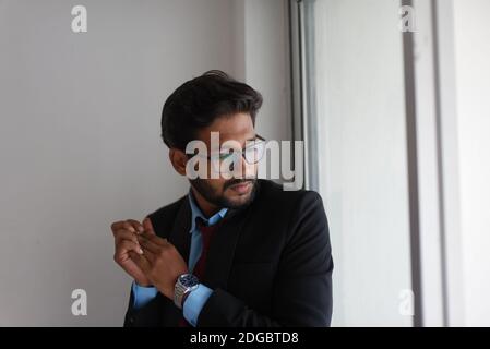 Portrait eines indischen Bengali großer, dunkler, hübscher Brünette junger Mann in Bürokleidung steht vor einem Glasfenster in einem Firmenbüro/bpo Stockfoto