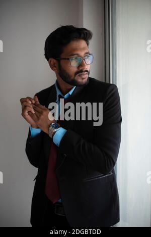 Portrait eines indischen Bengali großer, dunkler, hübscher Brünette junger Mann in Bürokleidung steht vor einem Glasfenster in einem Firmenbüro/bpo Stockfoto