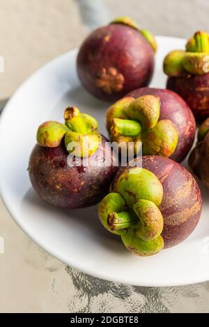 Frische Mangostan ganze Frucht liegt auf einem weißen Teller close-up Vertikales Foto Stockfoto