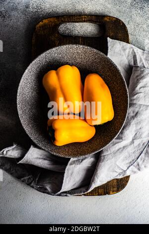 Ansicht von oben auf drei gelbe Paprika in einer Schüssel Auf einem Schneidebrett Stockfoto