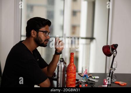 Ein indischer bengalischer großer, dunkler, hübscher, braunes Bartbraunet im lässigen T-Shirt sitzt in kreativer Stimmung auf einem Bürotisch. Stockfoto