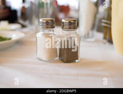 Salz und Pfeffer in einem transparenten Glasbehälter auf einem Tisch zur Mittagszeit auf einer weißen Tischdecke Spic Stockfoto
