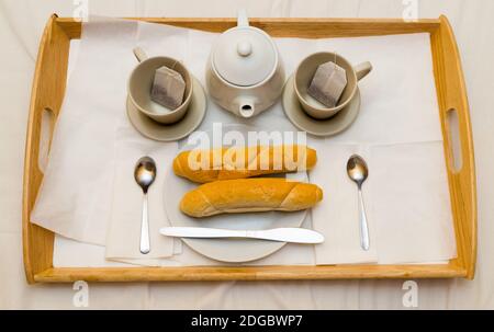 Gedecktes Frühstück für zwei auf einem Holztablett sind zwei Tassen Teekanne Baguettes auf frischen knusprigen Tellern Stockfoto