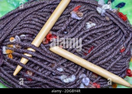 Stricknadeln und eine Wollgarnkugel auf dunkelgrauem Holzhintergrund. Dunkle Holzfäden und Stricknadeln Stockfoto