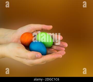 Drei Eier liegen in den Handflächen rot grün Blau auf braunem verschwommenem Hintergrund Stockfoto