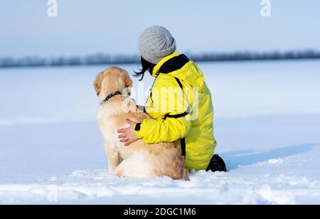 Rückansicht des freundlichen Hundes und der Frau, die auf verschneit sitzen Ein Stockfoto