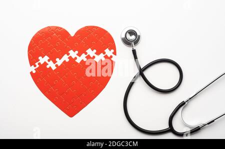 Stethoskop neben gebrochenen roten Herz geformt Puzzle Stockfoto