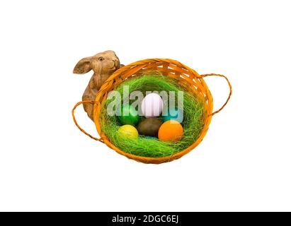 Grünes Nest mit bunten Eiern in einem Korb Holzkaninchen Figur auf weißem Hintergrund Stockfoto