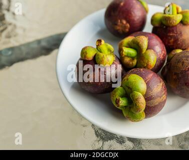 Frische runde Frucht Mangostan köstlich liegt auf einem Teller stehend Auf einem transparenten Tisch Stockfoto