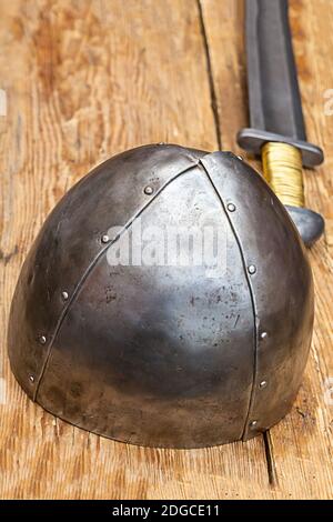 Eisenstahlhelm steht auf dem Hintergrund eines langen Schwert auf einem Holztisch Stockfoto