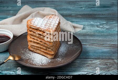 Ein Stapel herzförmiger Waffeln, bestreut mit Puderzucker auf einem hölzernen Hintergrund. Stockfoto