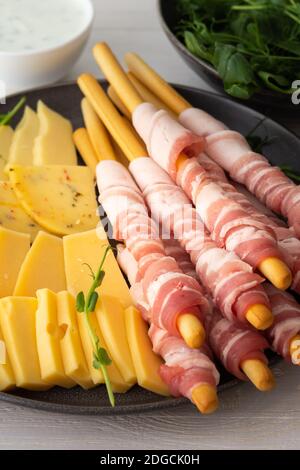 Grissini Brot mit Speck, verschiedene Käsesorten und Erbsensprossen, Soße und Spinat in der Nähe auf weißem Holzgrund Stockfoto