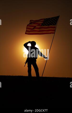 Silhouette von US-Armee Soldat, Marines Corps Kämpfer oder Spezialeinheiten Rifleman in Helm, bewaffnete Gewehr steht auf einem Hügel mit Winken auf Wind Nationalflagge, Blick weit weg auf den Hintergrund des Sonnenuntergangs Himmel Stockfoto