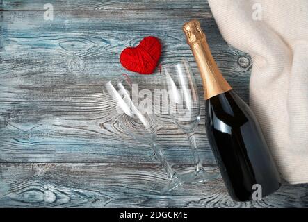 Eine Flasche Champagner, zwei Gläser und ein Herz auf einem Holzhintergrund mit einem Pullover. Stockfoto