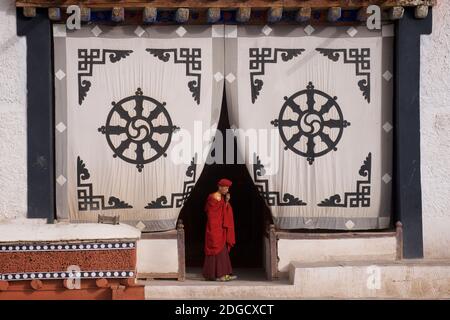 Am frühen Morgen im Hemis Kloster. Ein junger Mönch am Eingang des Gebetshauses. Auf dem Stoffschirm am Eingang oben ist die Dharmachakra - A Stockfoto