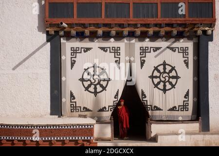 Am frühen Morgen im Hemis Kloster. Ein junger Mönch am Eingang des Gebetshauses. Auf dem Stoffschirm am Eingang oben ist die Dharmachakra - A Stockfoto