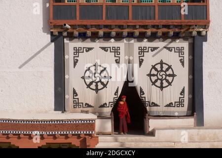 Am frühen Morgen im Hemis Kloster. Ein junger Mönch am Eingang des Gebetshauses. Auf dem Stoffschirm am Eingang oben ist die Dharmachakra - A Stockfoto