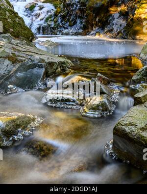 Schöner gefrorener Wasserfall im Winter. Es entsteht ein gefrorenes Wasserbecken. Felsen von Eis bedeckt, umgeben das Wasser Stockfoto