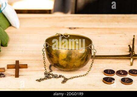 Metallschale für Bronzestände mit Kette steht auf Ein Holztisch neben den Münzen und ein Kreuz Stockfoto