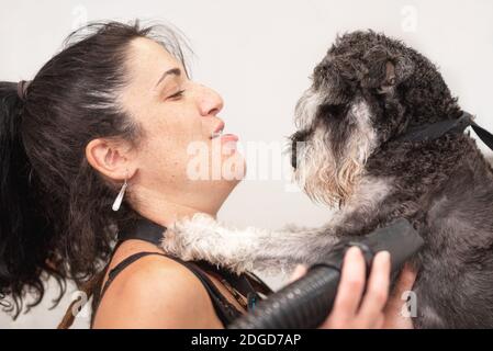 Hündin Pet Groomer umarmt zärtlich einen Schnauzer Hund im Pflegesalon. PET Liebe und Pflege Konzept. Stockfoto