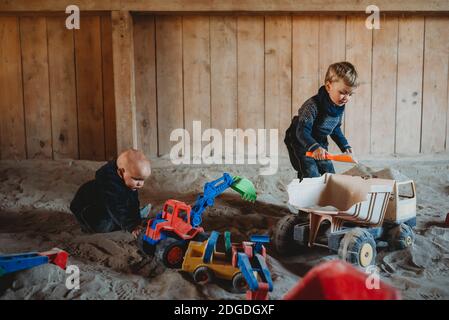 Kinder, die mit Lastwagen und Baggern im Sandkasten im Freien spielen Winter Stockfoto