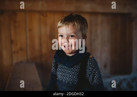 Entzückender kleiner Junge lächelt im Winter in einer Holzhütte Stockfoto