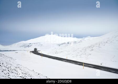 Fernes Fahrzeug auf kurviger Straße zwischen weiß verschneiten hügeligen Terrain im Winter Tag Stockfoto