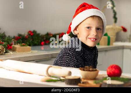 Boy 7-10 in einer Weihnachtsmütze, die Weihnachts-Lebkuchenkekse in der Neujahrsküche macht. Stockfoto