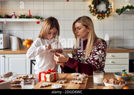 Mama helfen Kind Tochter machen Weihnachtskekse Dekorationen zu Hause. Stockfoto